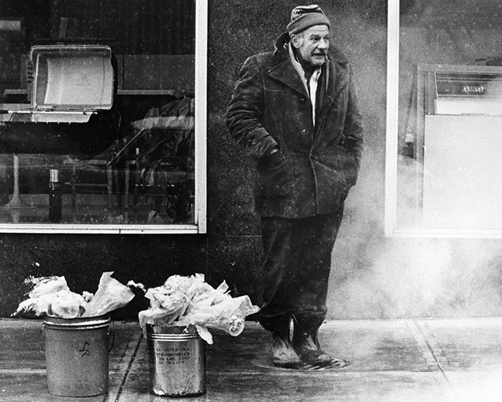 Homeless man selling flowers, standing on a grate, by William Wynne